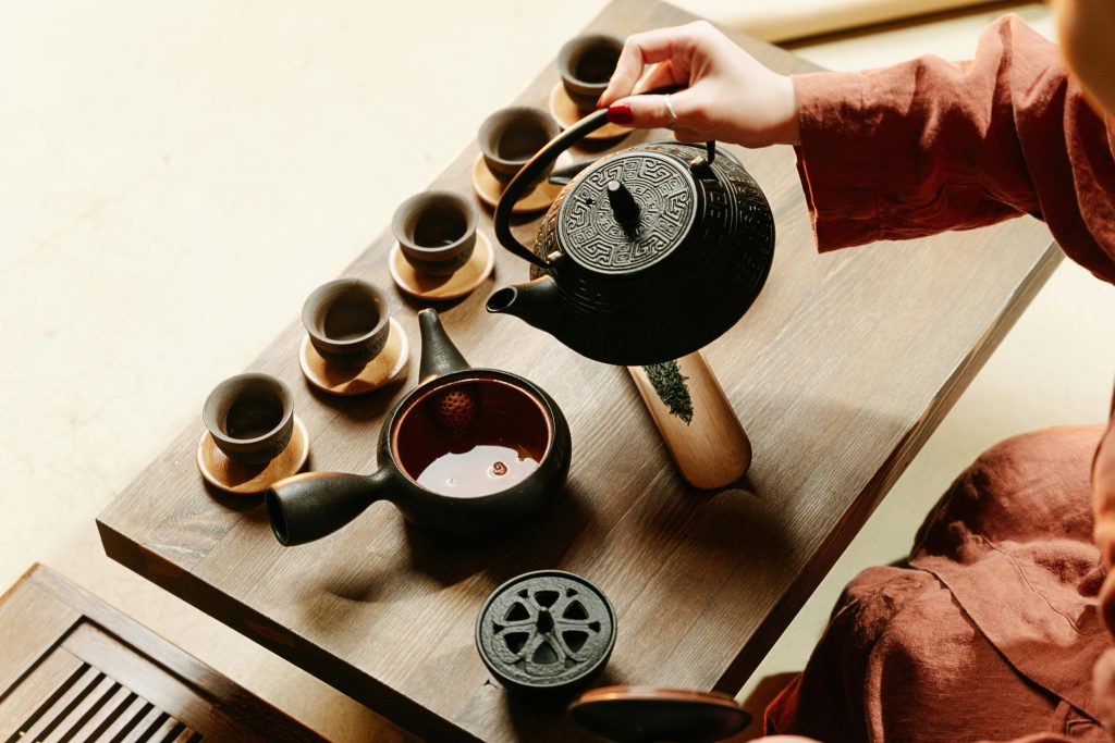 Traditional tea ceremony showcasing handmade teapot pouring tea into cups on a wooden tray.