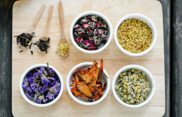 Colorful dried flowers and herbs displayed in bowls on a wooden board.